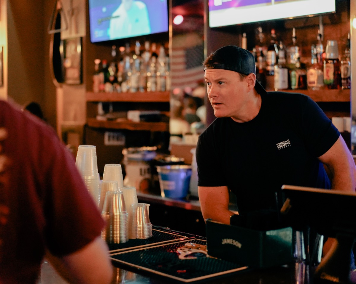 A bartender at a Denver bar checking in with a guest, cups stacked on the counter