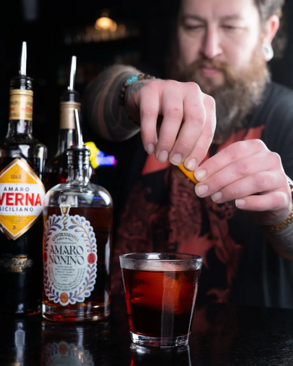 A bartender crafting a cocktail with amaro bottles on the bar