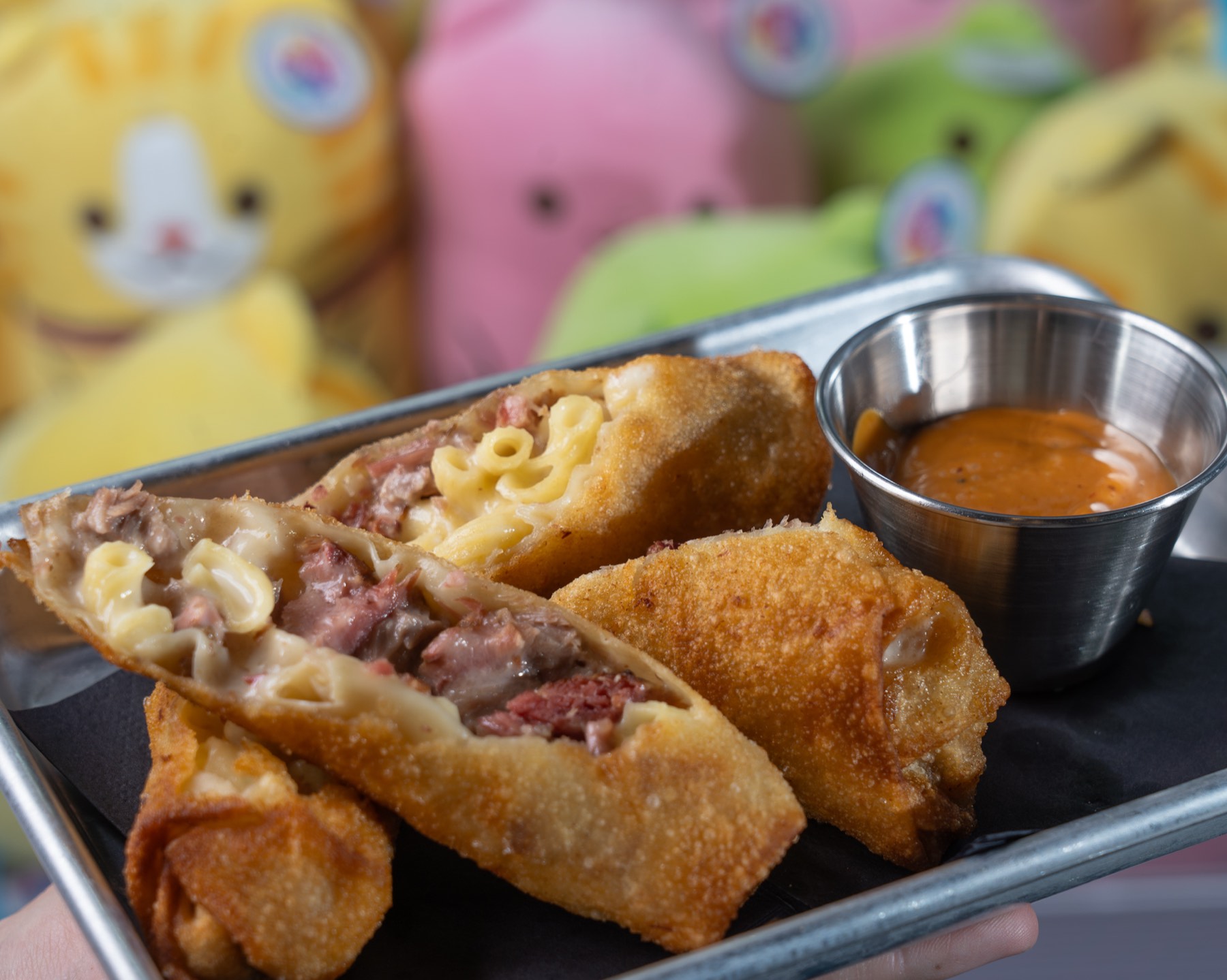 Crispy egg rolls plated with dipping sauce against a colorful claw machine backdrop