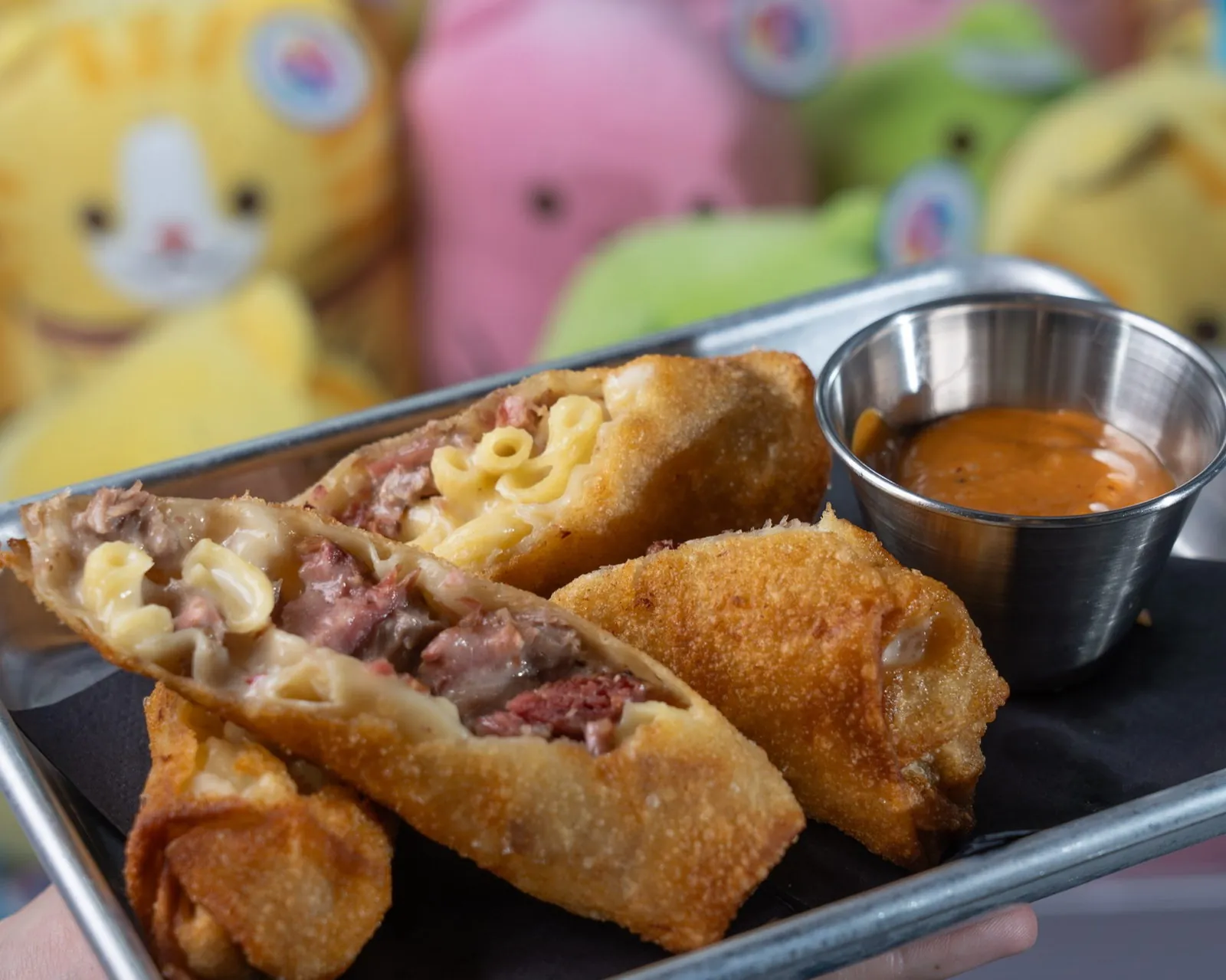 Crispy egg rolls plated with dipping sauce against a colorful claw machine backdrop
