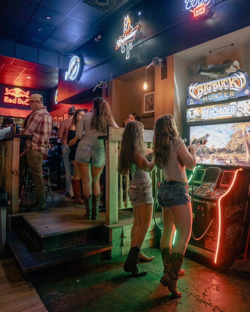 Two guests playing an arcade game under neon signage at a Denver bar