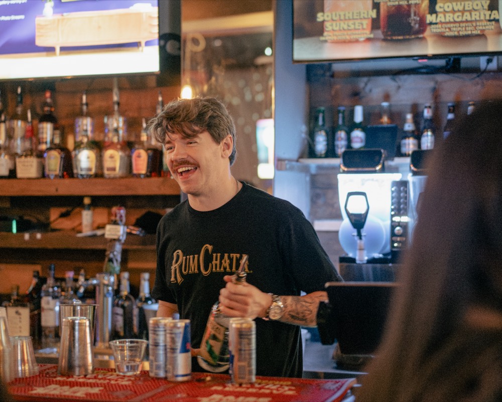 A bartender laughing while pouring a drink behind the bar