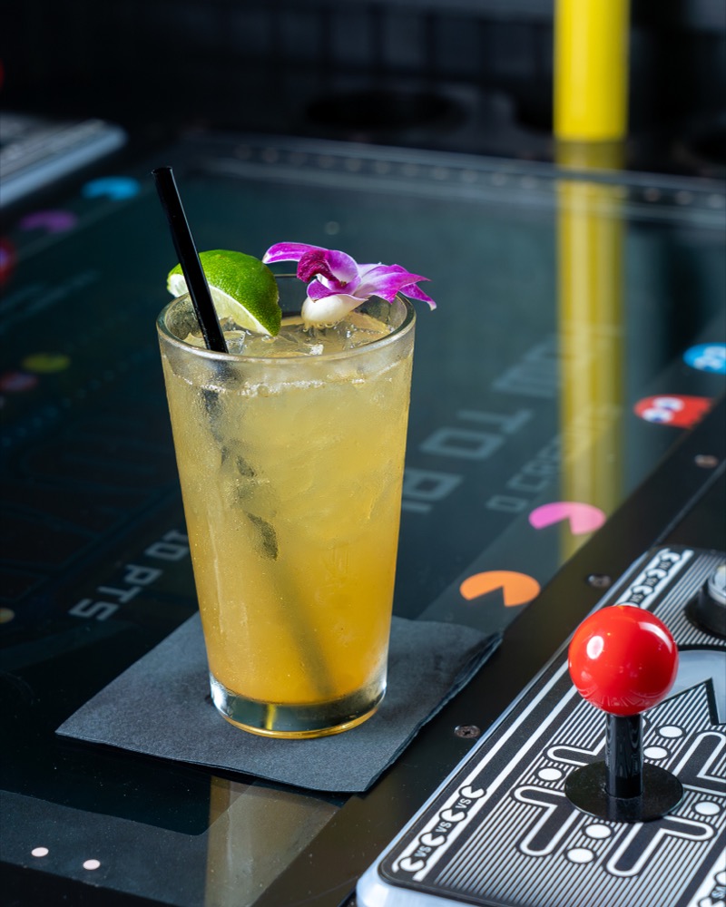 Craft cocktail styled against an arcade cabinet