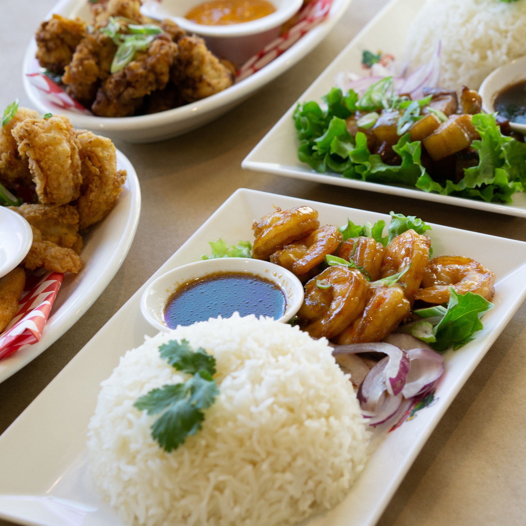 A close-up spread of glazed shrimp, fried chicken, and pork bites plated with rice at a restaurant table