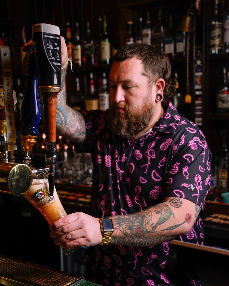 A bartender in a black apron building a cocktail behind a Denver bar
