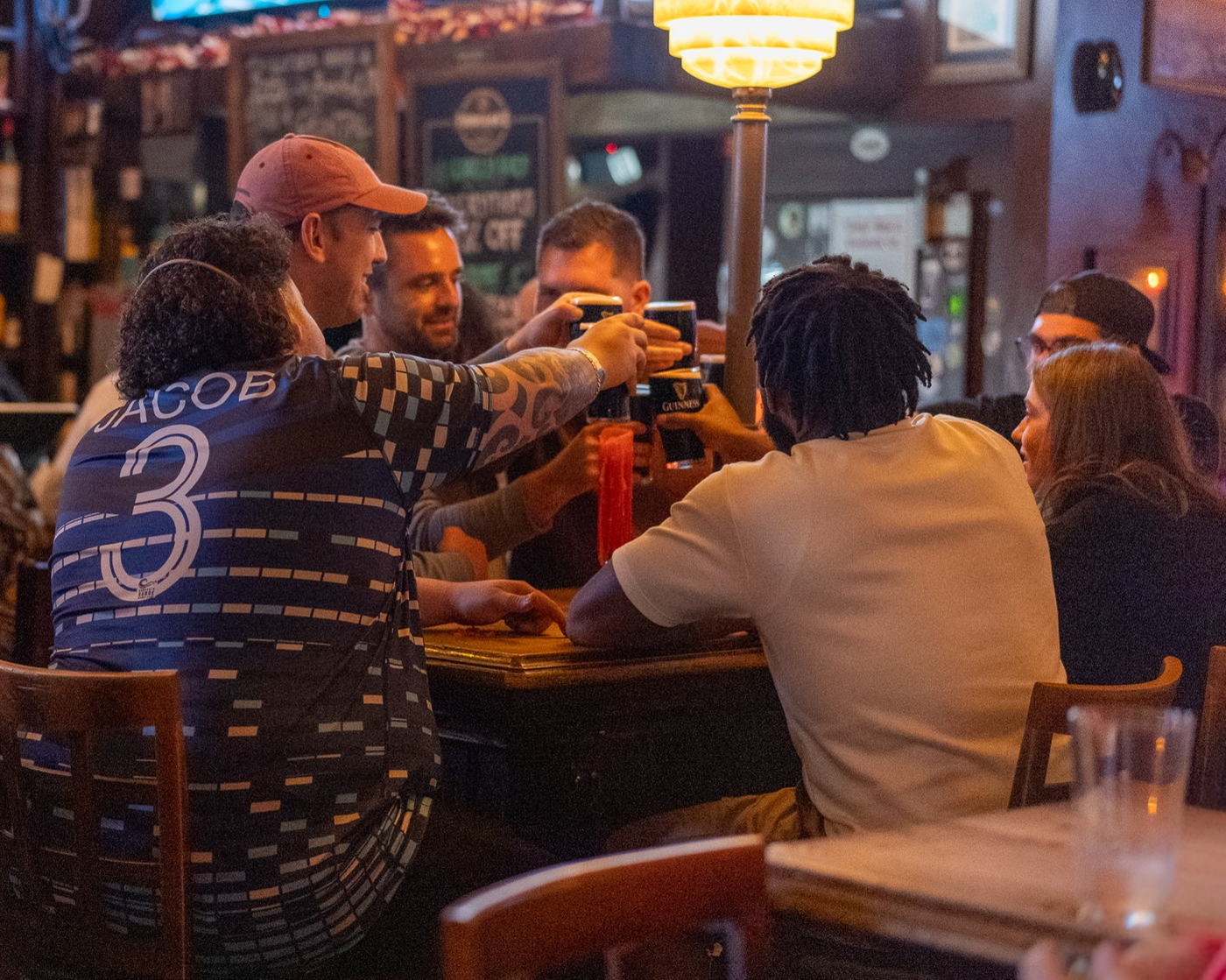 A group of friends toasting drinks together at a crowded bar table