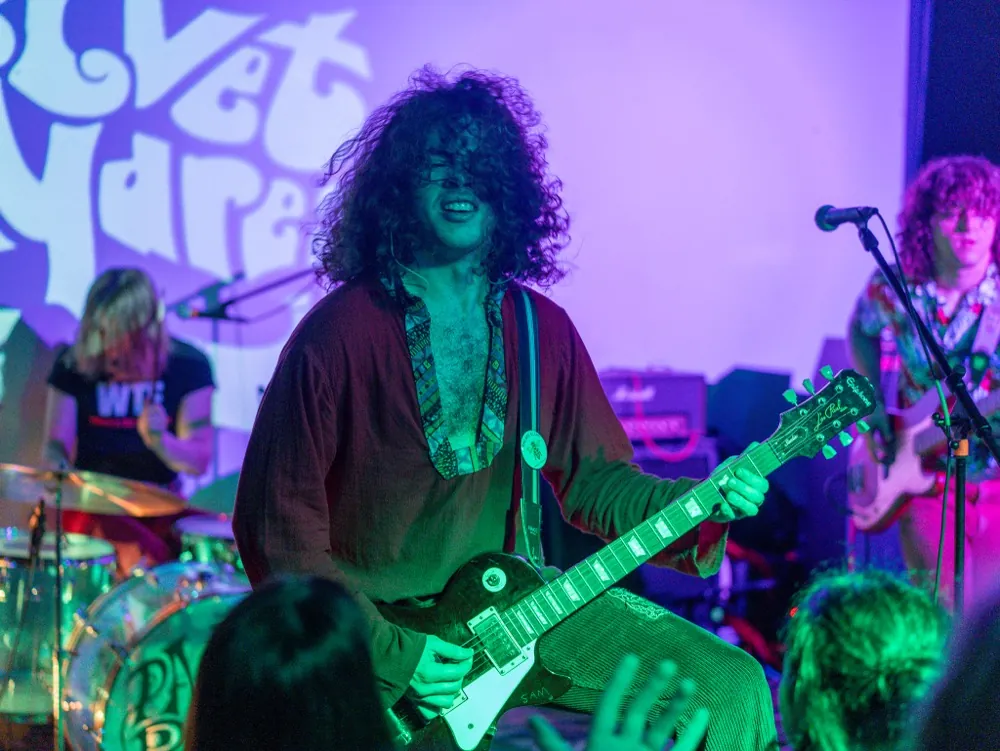 A band performing under green and purple stage lighting