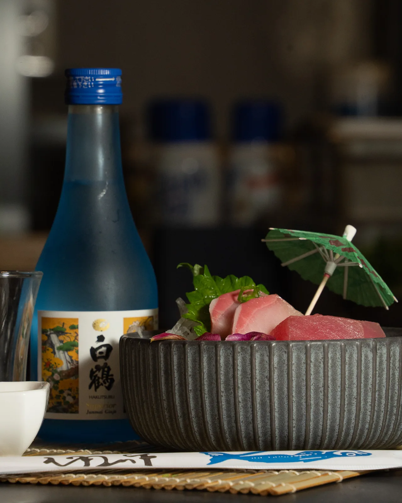 Sashimi on ice in a ribbed stone bowl, served beside a bottle of sake in a dim dining room