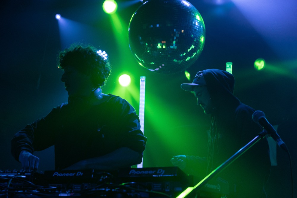A DJ silhouetted under green stage lighting and a disco ball