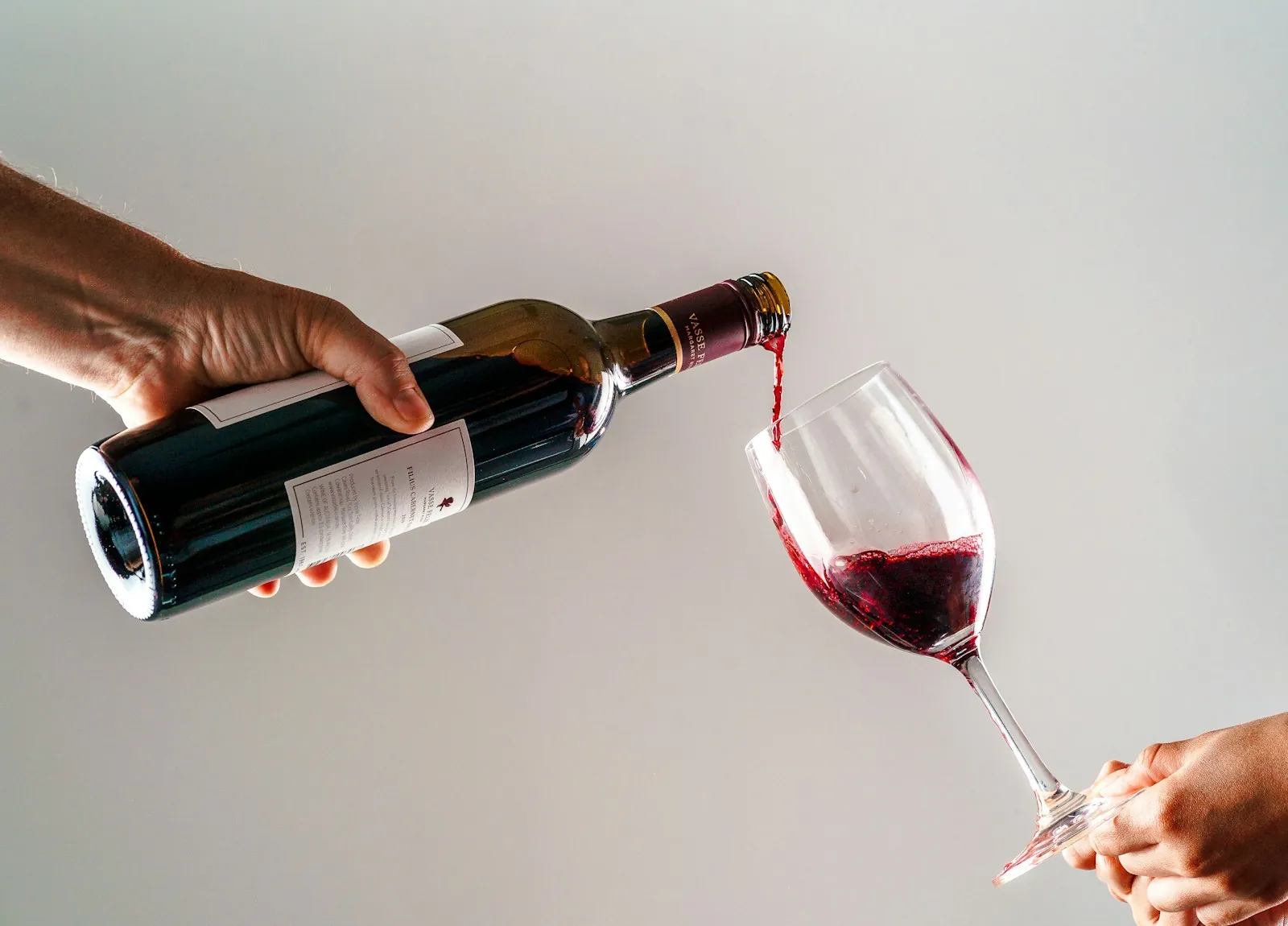 Red wine poured from a bottle into a glass held out for a tasting